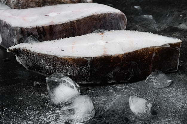 Frozen fillets of white fish, pollock set, on black dark stone table background, with copy space for text