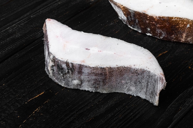 Frozen halibut steak on black wooden table background with copy space for text