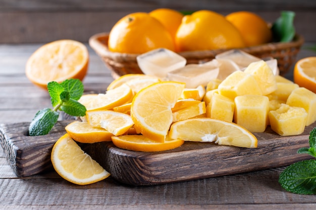 Frozen lemon slices and cubes of lemon juice on a cutting board on a wooden table, frozen fruits