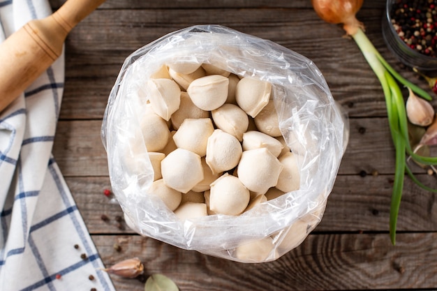 Frozen meat dumplings in a plastic bag on wooden background