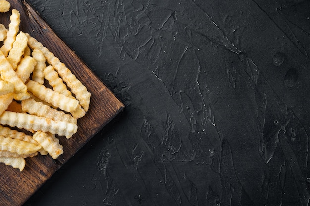 Frozen oven chips sliced potato set, on wooden cutting board, on black background, top view flat lay , with copyspace  and space for text