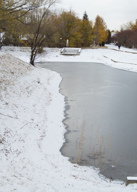 Frozen pond covered with the first snow in the city Park