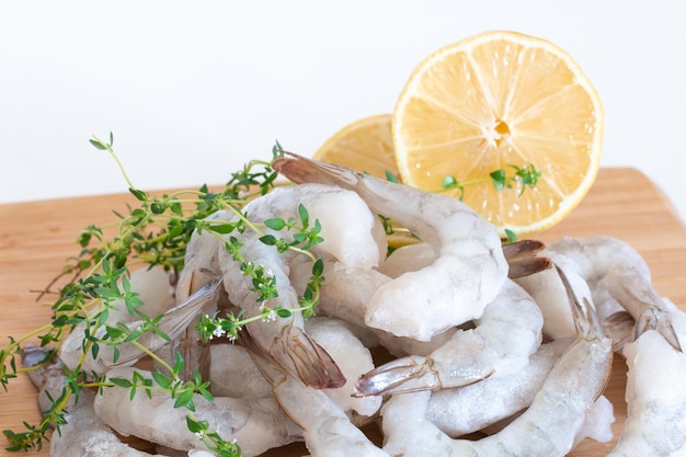 Frozen raw shrimps peeled on a wooden cutting board with herbs and lemon