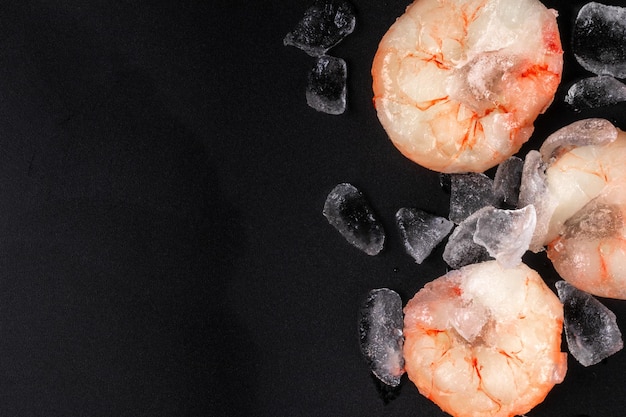 Frozen red raw cooked or uncooked shrimps and prawns with ice on black background top view