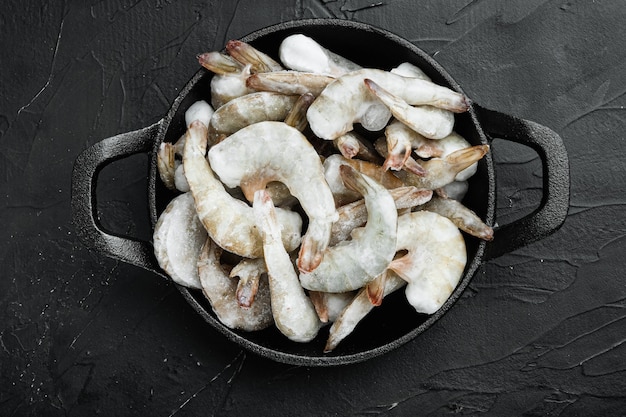 Frozen shell on Tiger Prawns or Asian tiger Shrimps set, in cast iron frying pan, on black stone table, top view flat lay