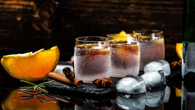 Frozen shot glass alcoholic drinks on rustic wood background Shot glass of herb liqueur with cinnamon and oranges on a dark background catering banner menu recipe place for text