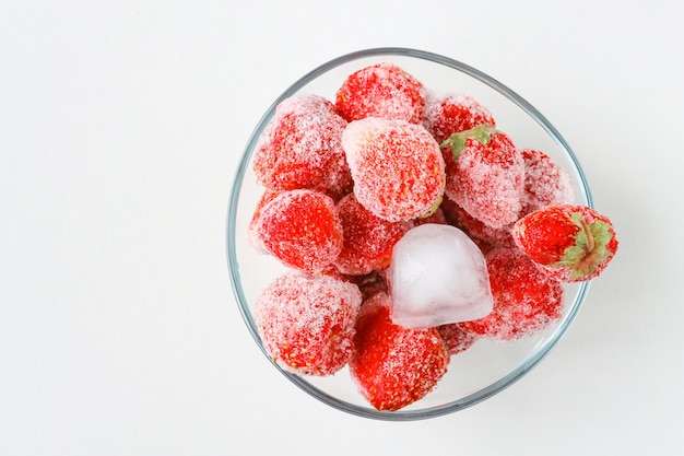 Frozen strawberries with ice cubes in a glass container top view