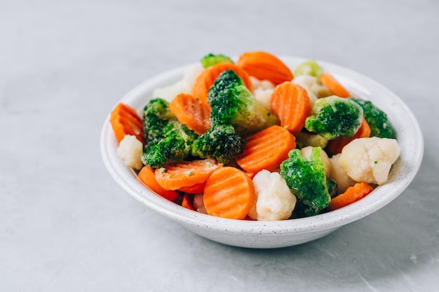 Frozen vegetables Frozen carrots broccoli and cauliflower in bowl on gray stone background