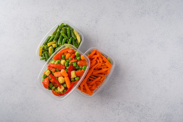 Frozen vegetables mix carrot broccoli spinach green pods beans in plastic trays on light surface