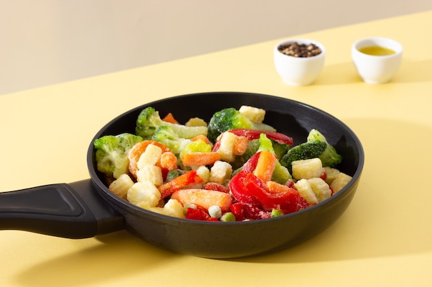 Frozen vegetables on the pan: paprika, carrot, broccoli, mini corn, tomato and green pea, pepper spices and olive oil in the background.