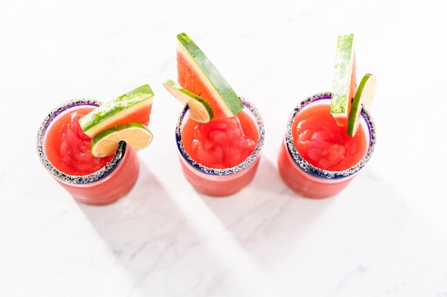 Frozen watermelon margarita in a glass garnished with salt a slice of fresh watermelon and lime