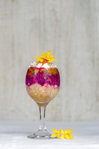 Fruit breakfast in a glass of oatmeal red dragon fruit passion fruit mango and honey in white wooden background closeup The concept of healthy eating