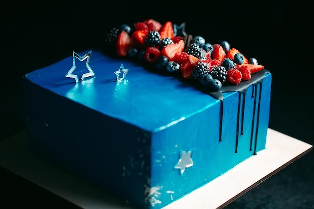 Fruit cake. Cake decorated with berries on a wooden stand on a black background