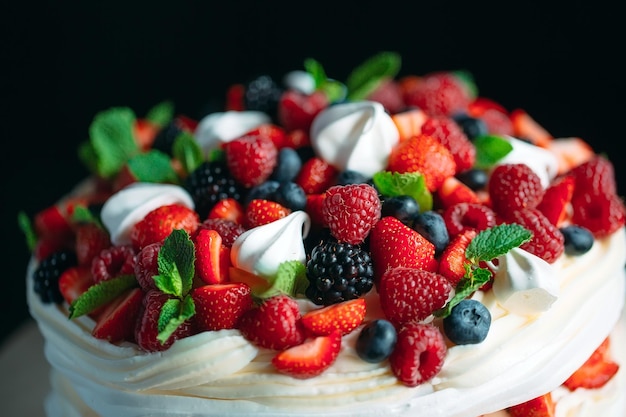 Fruit cake. Cake decorated with berries on a wooden stand on a black background.