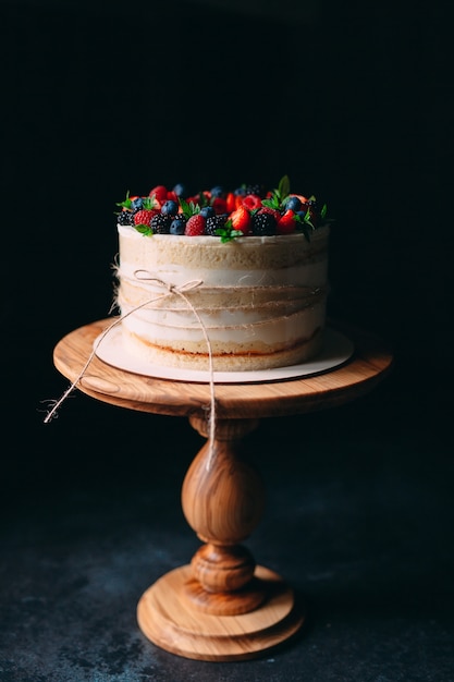 Fruit cake. Cake decorated with berries on a wooden stand on a black .