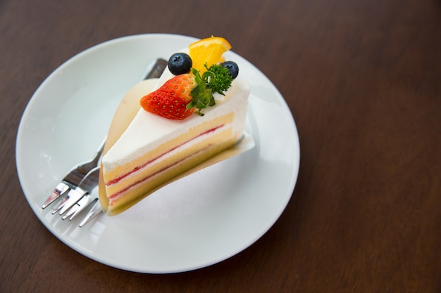 Fruit cake with whip cream topping strawberry and blueberry and orange on wooden table