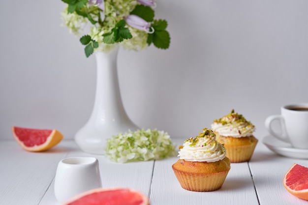 Photo fruit cupcakes for breakfast. morning table with dessert, espresso, grapefruit and flowers in a vase on a white wooden table.