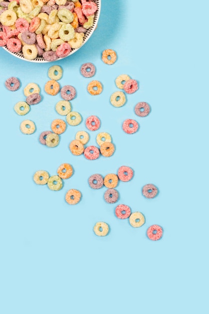 Fruit flavor colored cereals in a bowl and on a light blue background with copy space