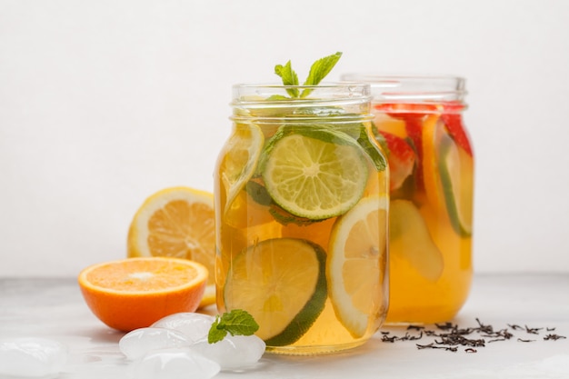 Fruit ice tea and ginger herbal ice tea with mint in a glass jars, white background, copy space. Summer refreshing drink concept.