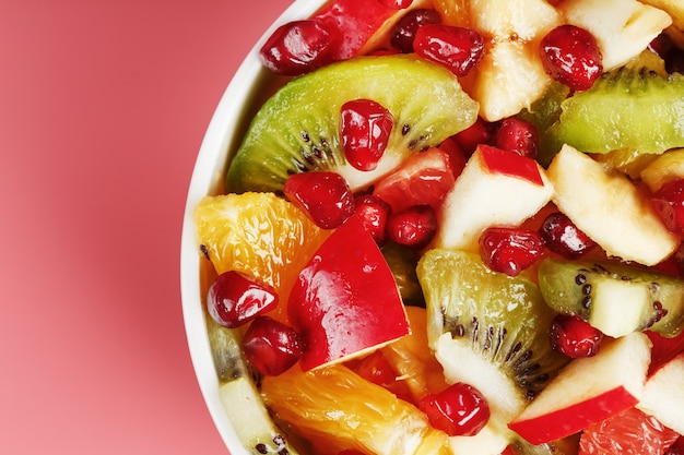 Fruit salad in a cup on a pink table. Slices of fresh, juicy and healthy fruits