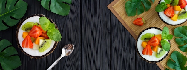 Fruit salad in the half coconut on the black wooden background Banner Top view