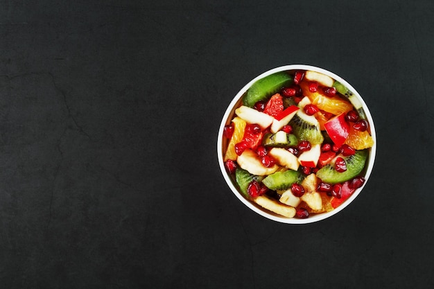 Fruit salad in a white cup on a black background, free space for text. Slices of fresh, juicy and healthy fruits for a healthy diet.