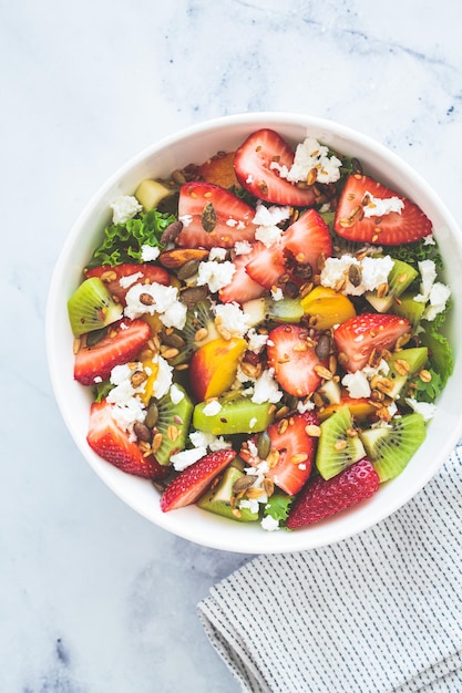 Fruit salad with feta and seeds in white bowl on white table Healthy vegan detox summer recipe