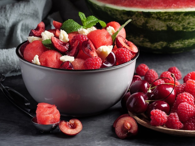 Fruit salad with watermelon, feta cheese, mint, raspberries and cherries on a gray background