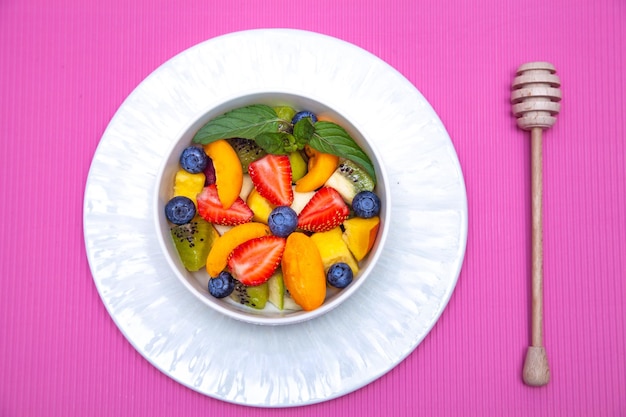 Fruit salad with wooden honey spoon on pink background