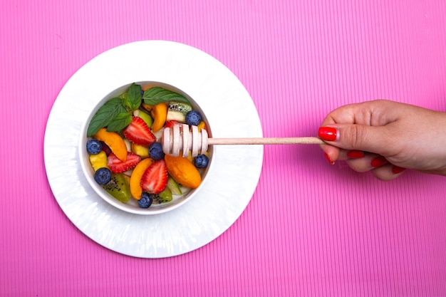 Fruit salad with wooden honey spoon on pink background