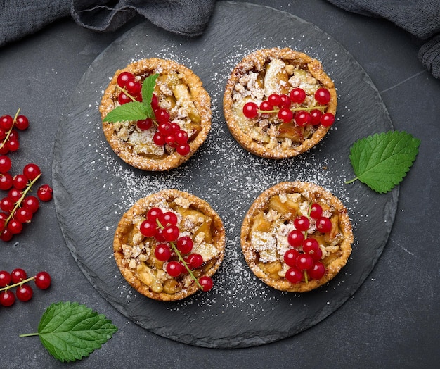 Fruit tart with red currants sprinkled with powdered sugar on a black table