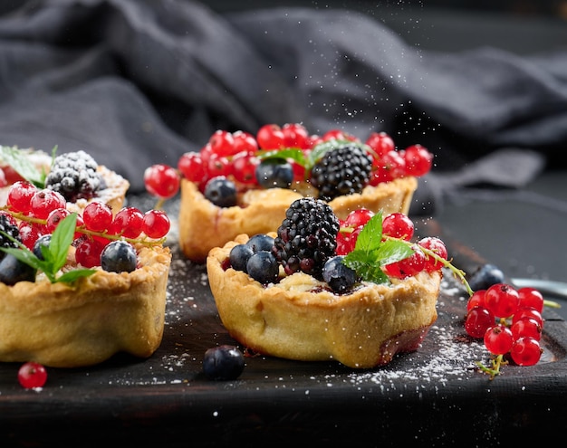 Fruit tart with red currants sprinkled with powdered sugar on a black table