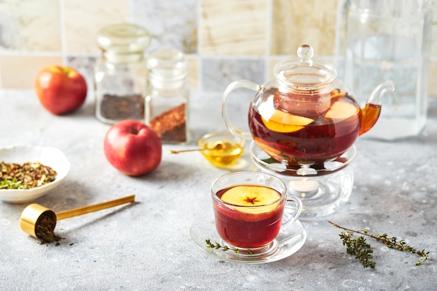 Fruit tea with apples and thyme in glass teapot and cup on the kitchen table