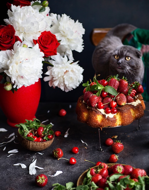 Fruitcake with orange, merry and strawberry with peonies and roses as a decoration and a cat behind