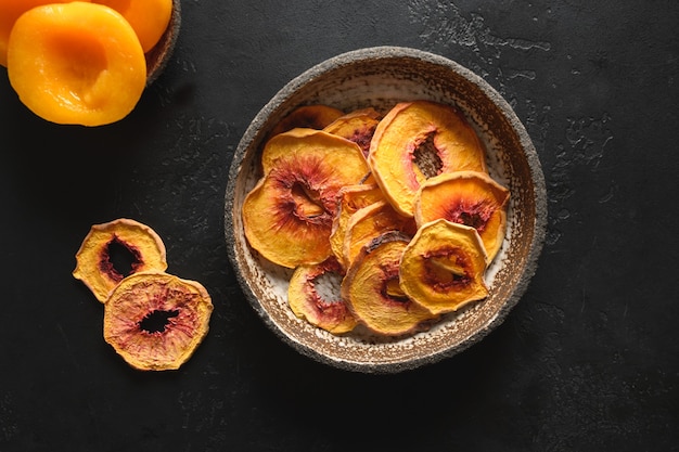 Fruits peach chips in bowl on black