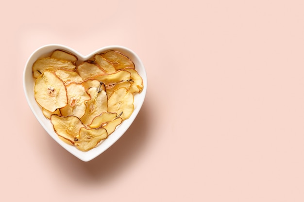 Fruits pear chips in plate shaped of heart on a pink background