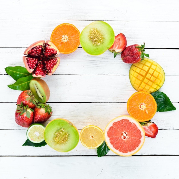 Fruits on a white wooden background. Mango, melon, pomegranate, strawberry, banana. Top view. Free space for your text.