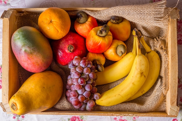 Fruits in wooden basket: cashew, orange, grape, banana, mango and papaya