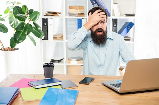 Frustated man clutching head working at laptop in office frustration