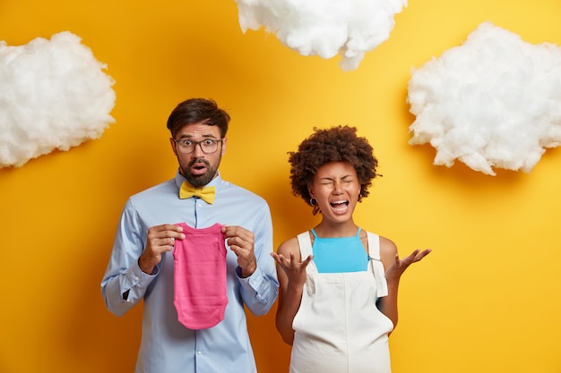 Frustated panic pregnant woman going to give birth cries from despair afraids of childbirth shocked husband prepares stuff for maternity home holds baby sleeper. Future parents. Family concept