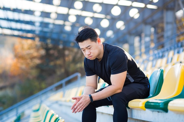 Frustrated Asian male athlete depressed dissatisfied with the result of his training in despair after running resting sitting