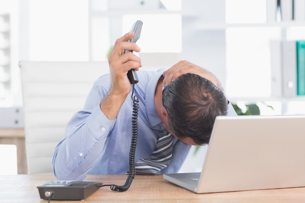 Frustrated businessman phoning at his desk 