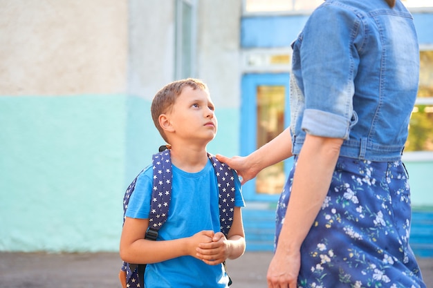 Frustrated Caucasian schoolboy with a backpack looks sadly at his mother