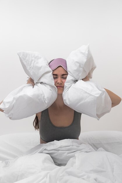 Frustrated lady tormented by noise clutches pillows to her ears battling insomnia and headache