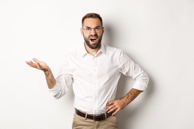 Frustrated office worker complaining, gesturing and looking disappointed, standing over white background.