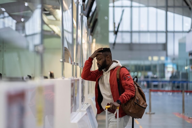 Frustrated sad young African man passenger having problems with checkin for flight