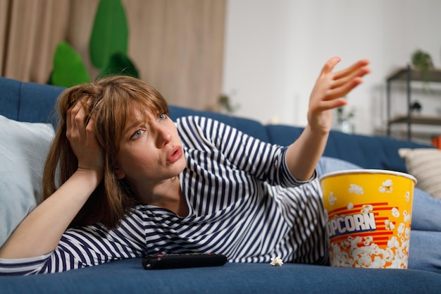 Frustrated woman watching TV while sitting on sofa in home