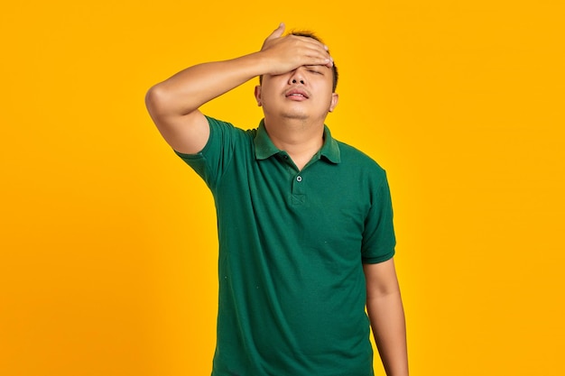 Frustrated young Asian man holding face with a hand on yellow background