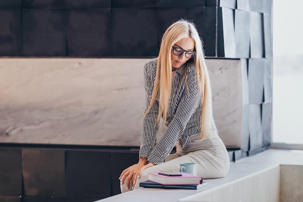 Frustrated young Swedish woman with loose long hair in glasses sitting on bath looks down tired after remote working at home Gorgeous Caucasian entrepreneur female feels fatigue Mockup