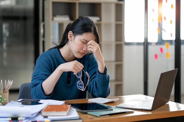 Frustrated young woman feeling tired and stressed keeping eyes closed and massaging nose while sitting at her working place